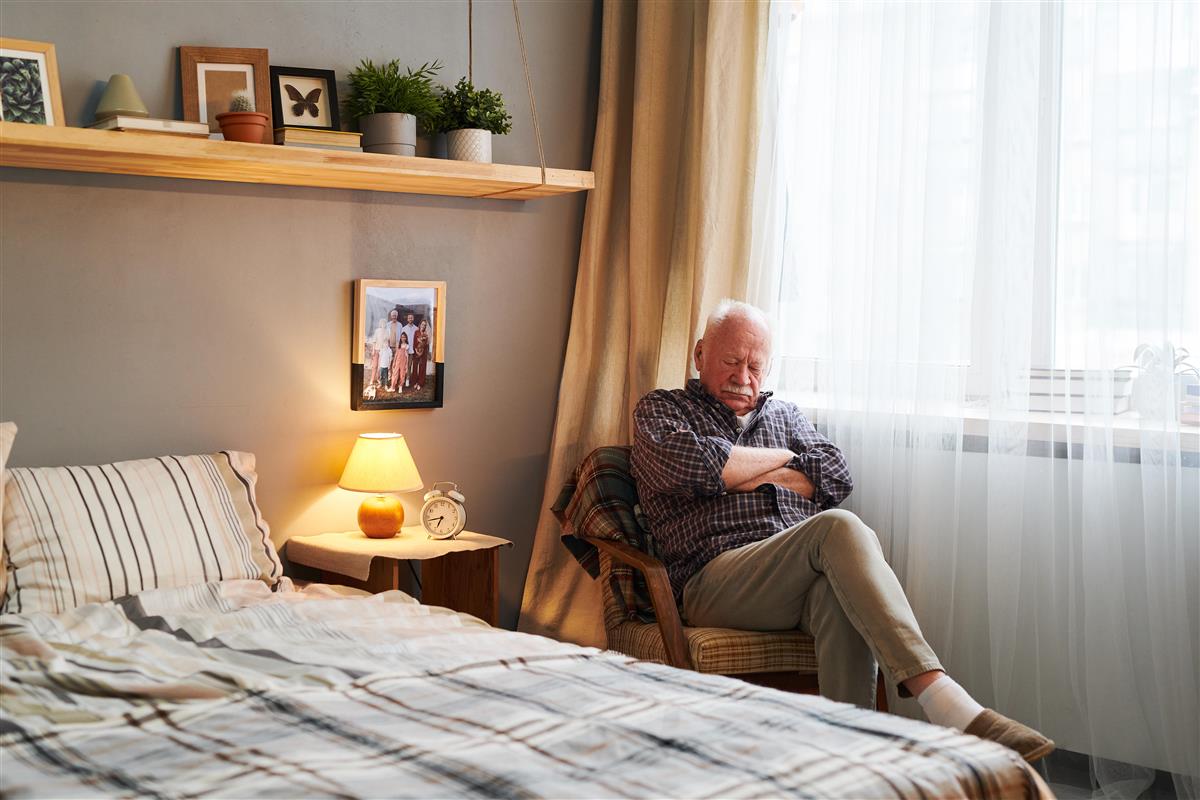 Eldre herremann har sovnet i stolen ved senga - Klikk for stort bilde
