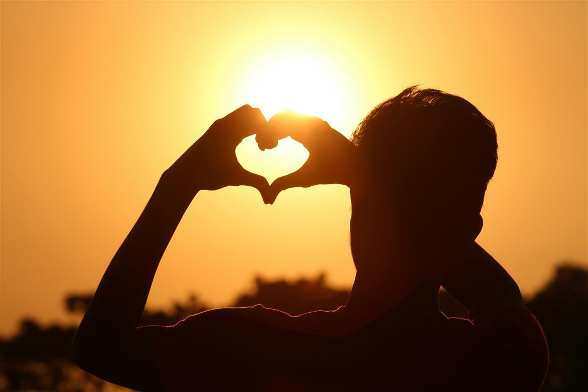 En person lager hjerte med hendene foran sola - Klikk for stort bilde