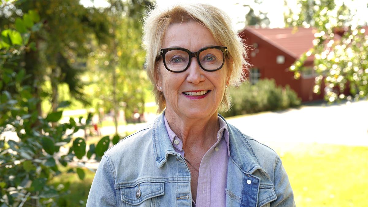 Dame med briller står foran et tre og smiler til kameraet - Klikk for stort bilde